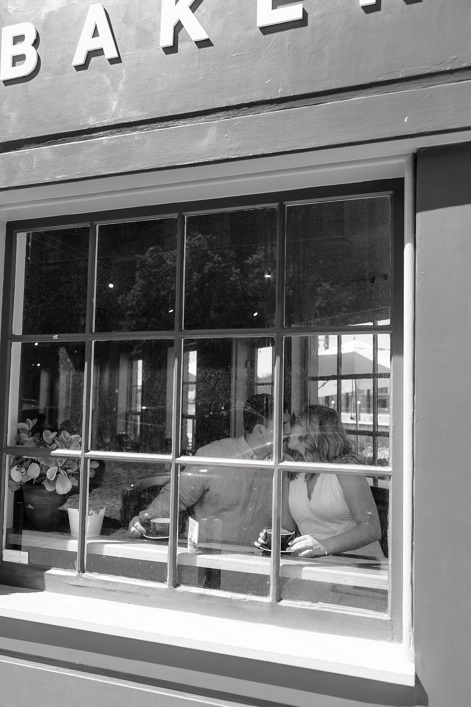 man and woman share a kiss behind a coffee shop window by Maryland wedding photographer