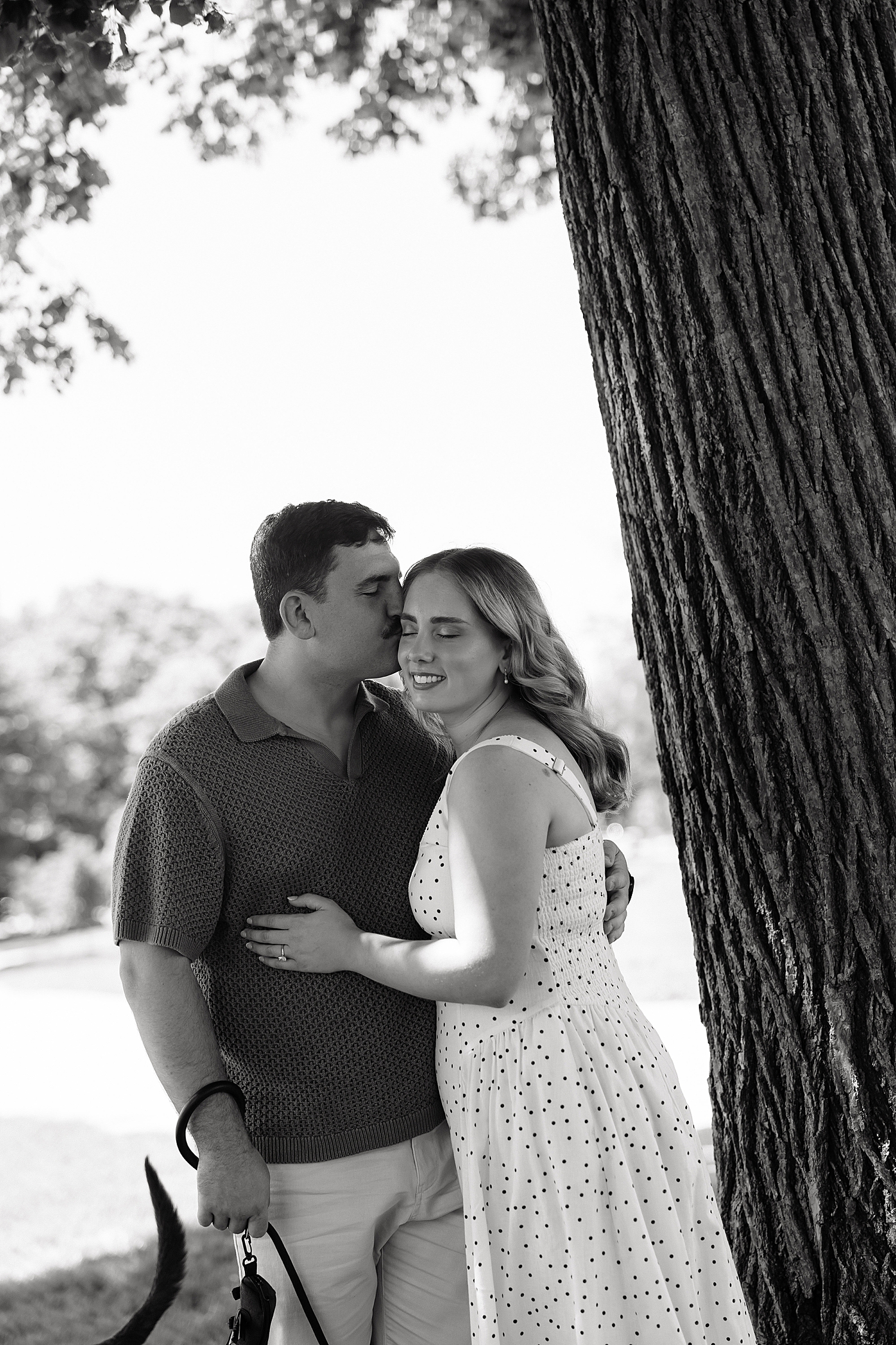 groom to be leans in to kiss woman next to tree by Maryland wedding photographer