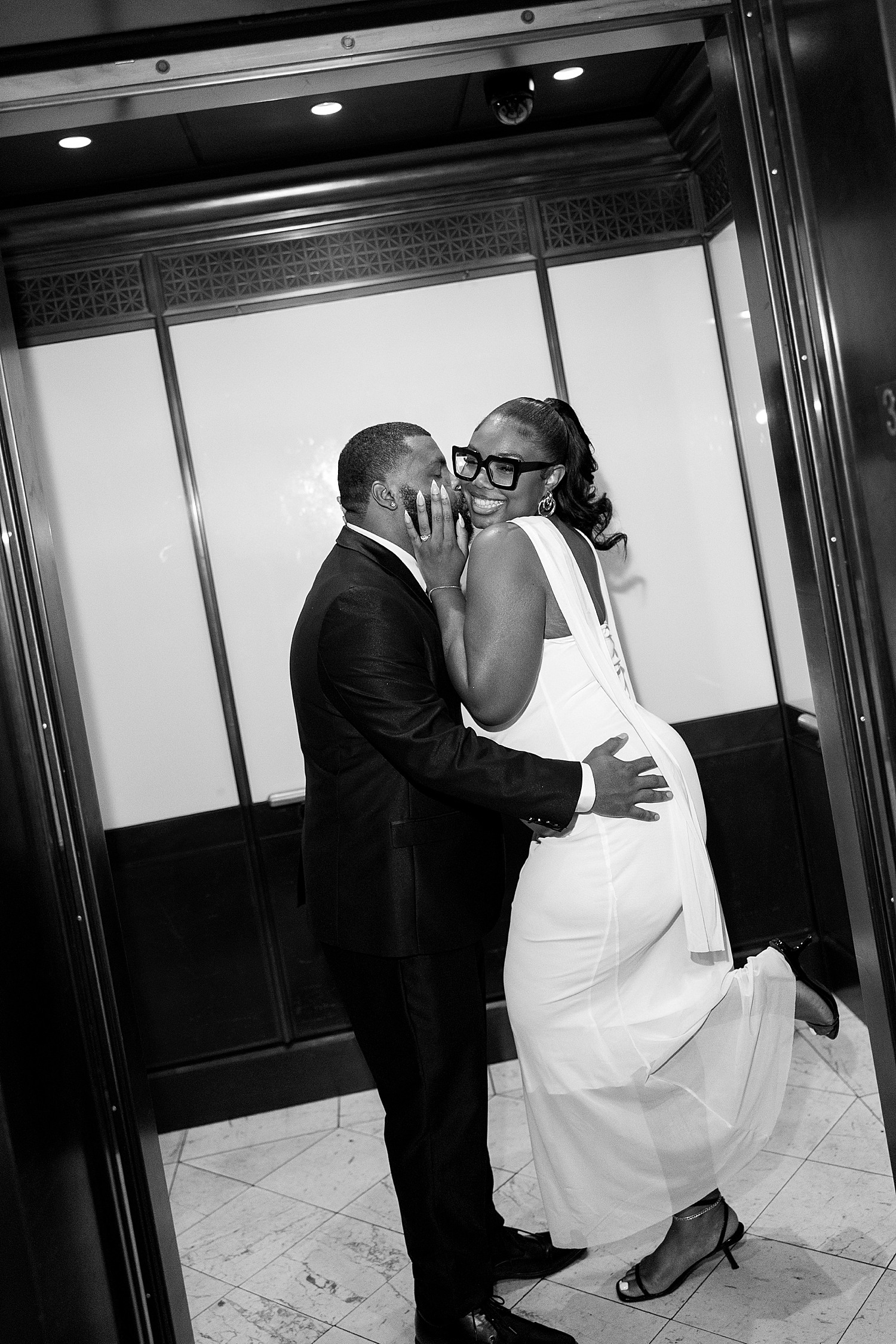 woman giggles as man kisses her neck in elevator by Sharp Impressions Photo