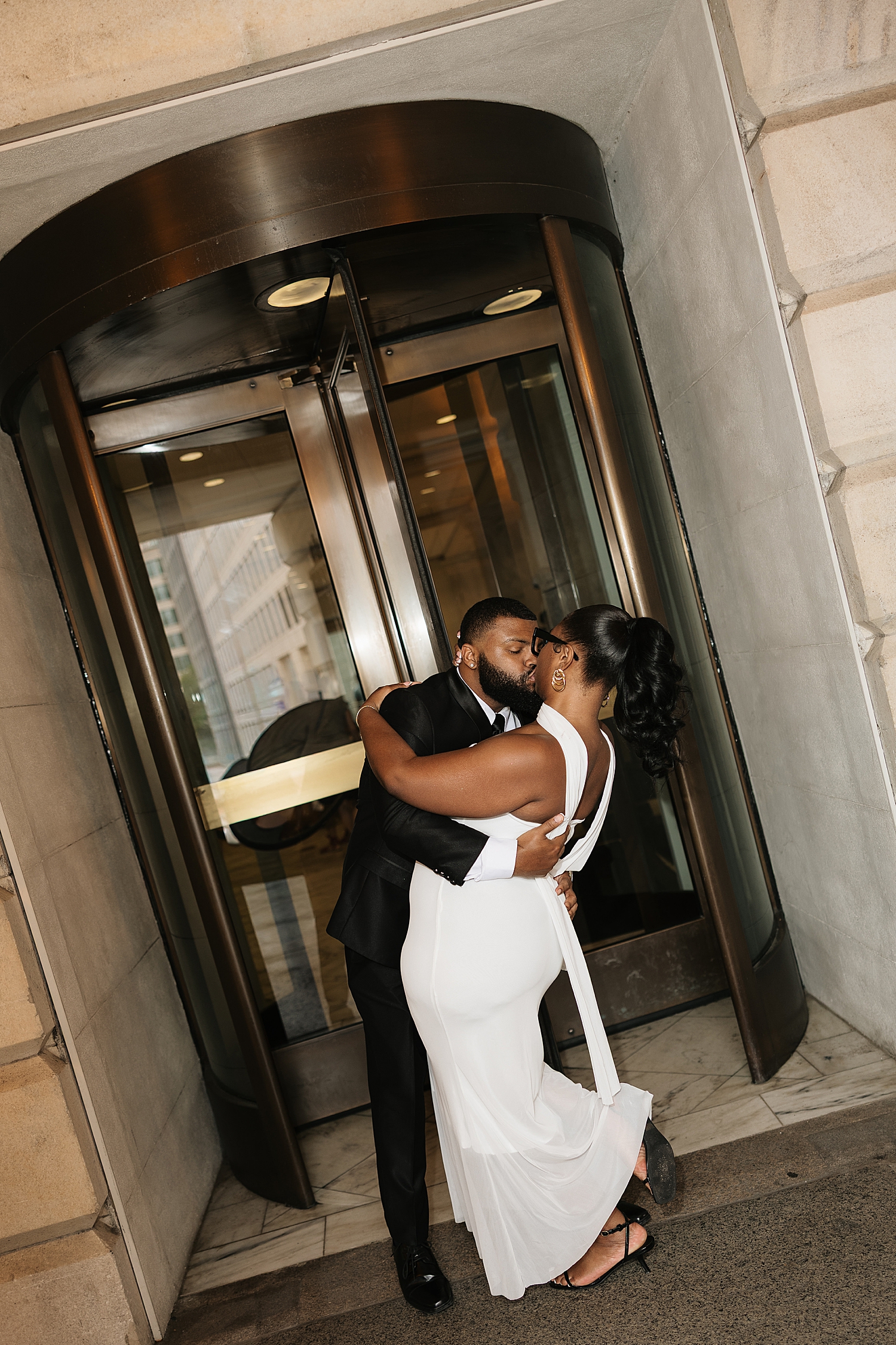 groom to be dips woman for a kiss outside of revolving doors by Sharp Impressions Photo