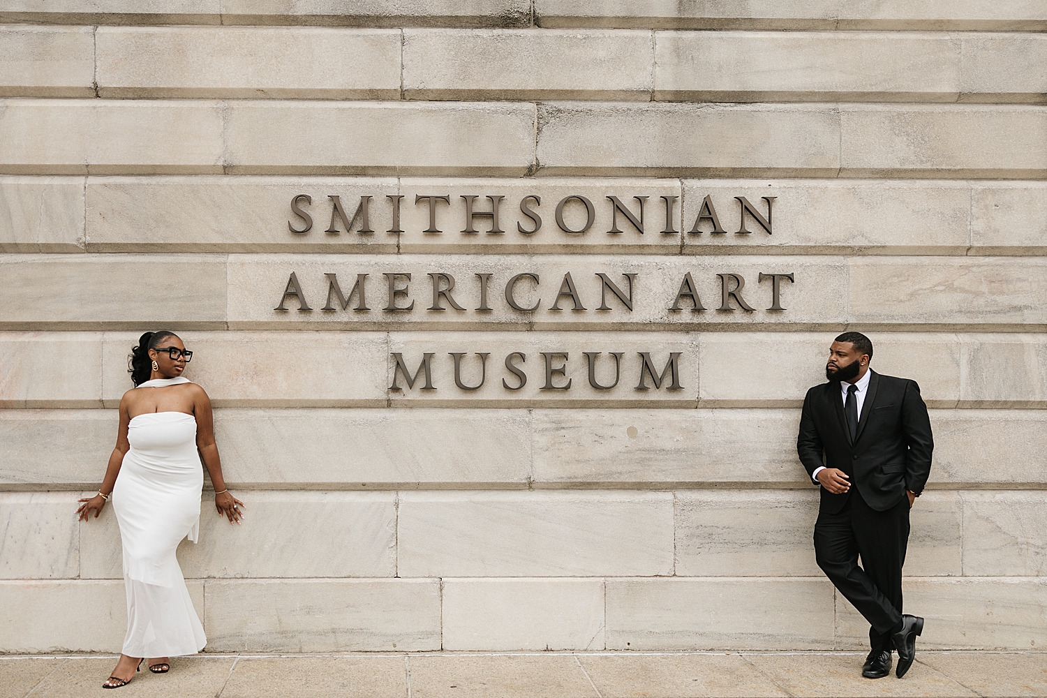 engaged couple stand on either side of sign outside of National Portrait Gallery