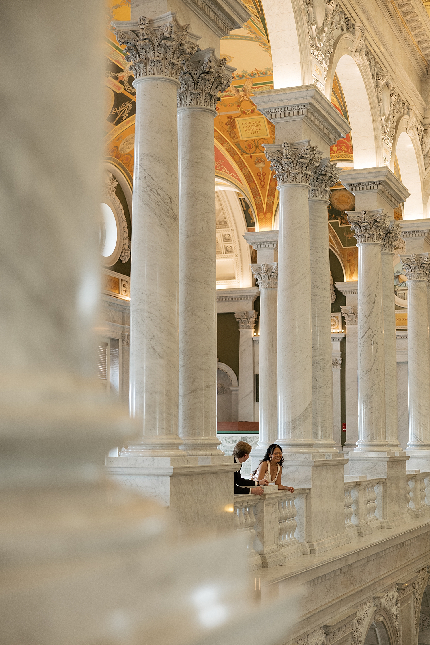 couple lean over grand balcony and talk together at The Library of Congress