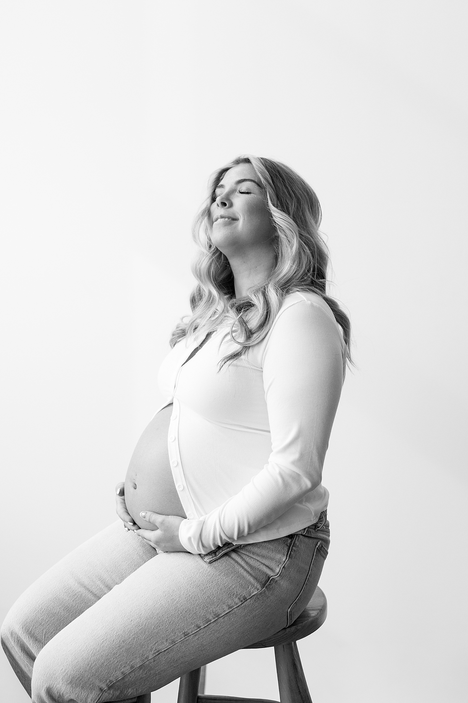 woman in open button down cradles bump, eyes closed by Sharp Impressions Photography