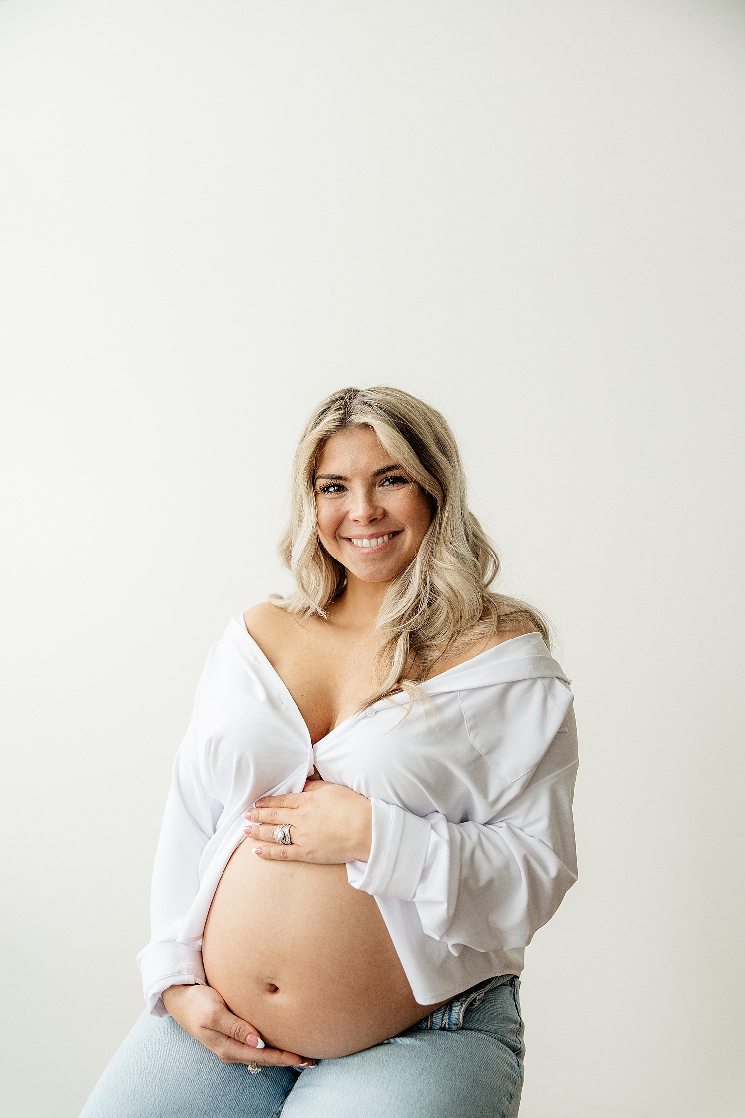 blonde woman in white button down cradles her bump by Maryland family photographer