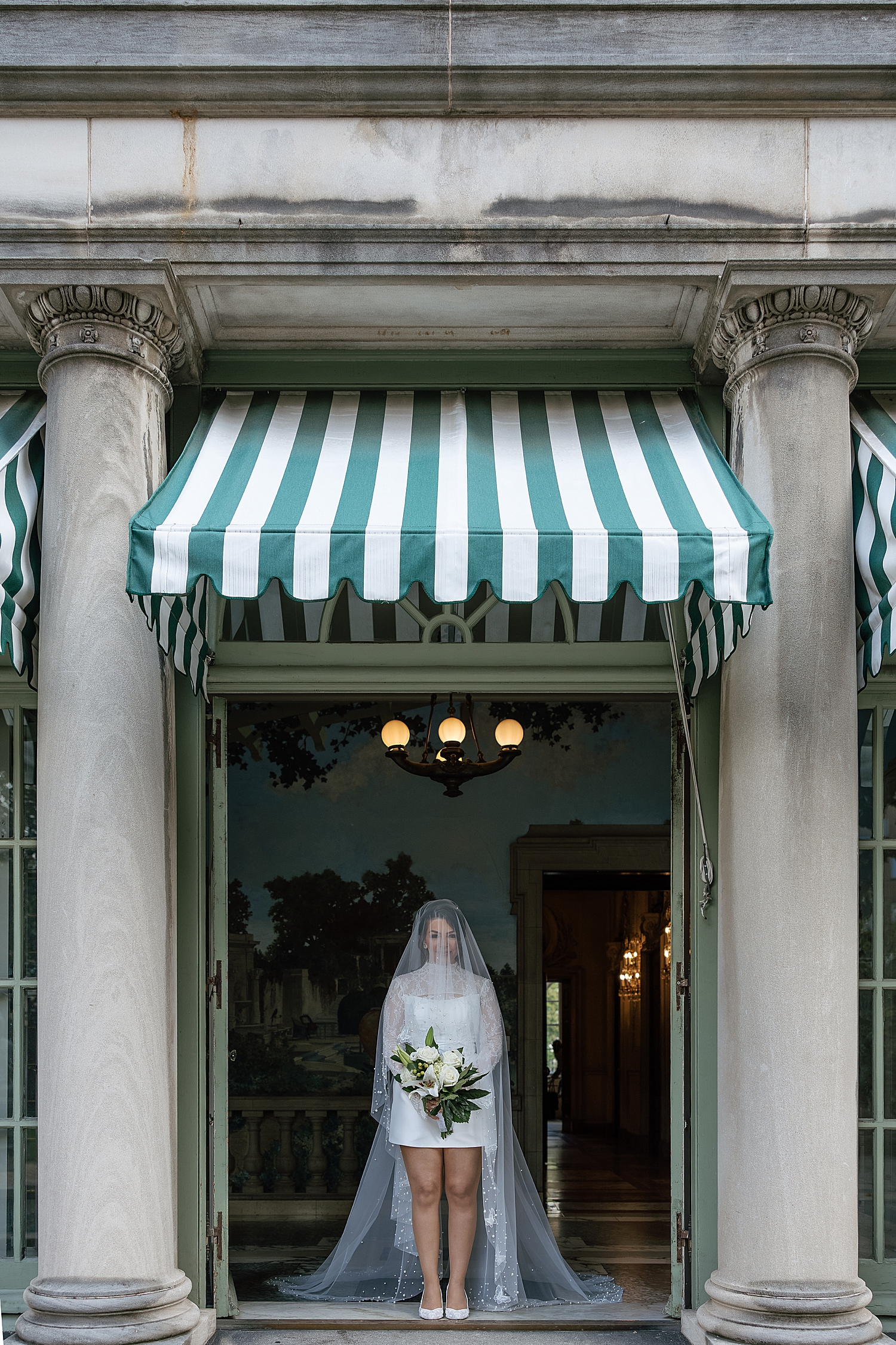 bride stands under green and white striped awning by Maryland wedding photographer