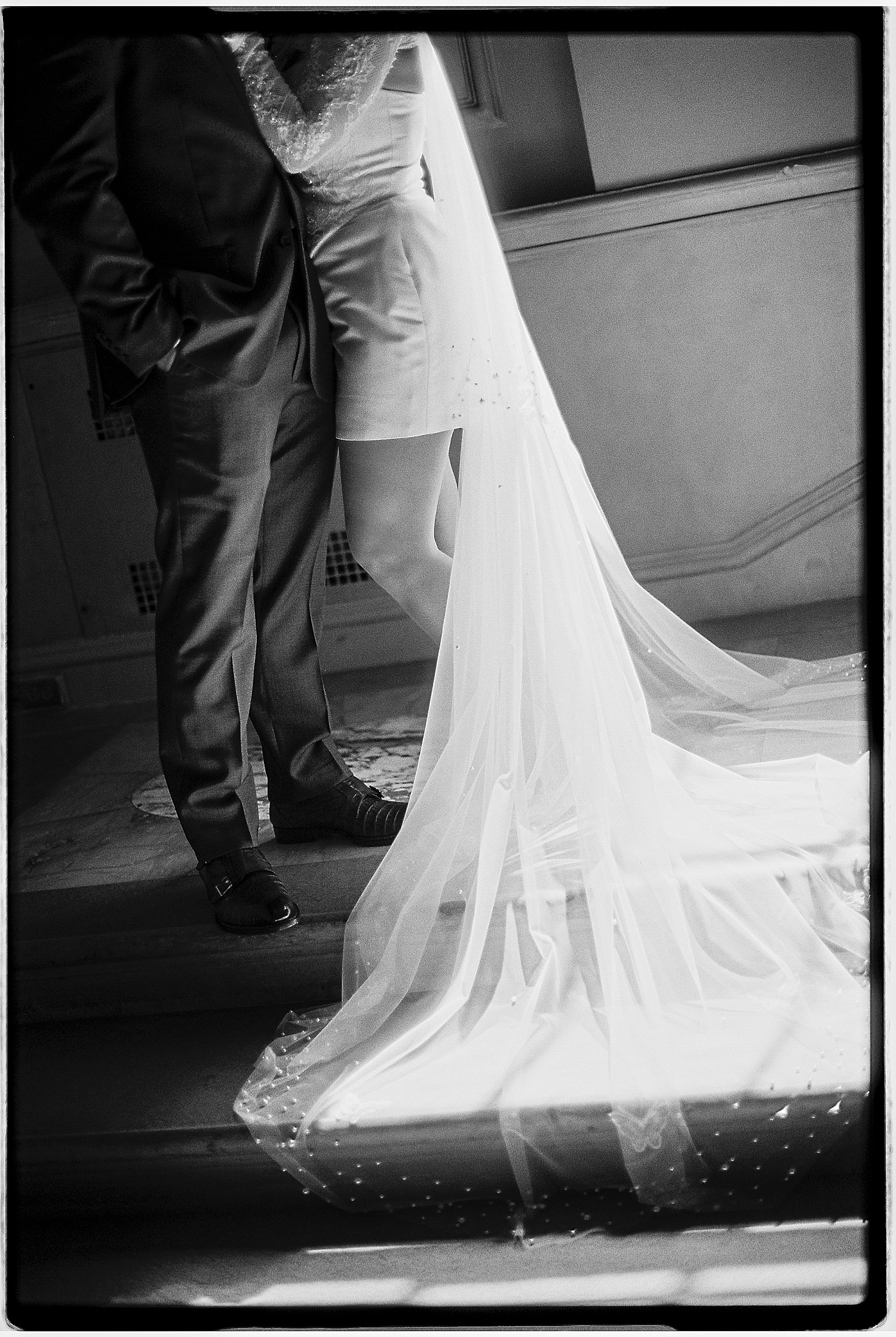 woman in mini dress and veil stands next to man in suit by Sharp Impressions Photography