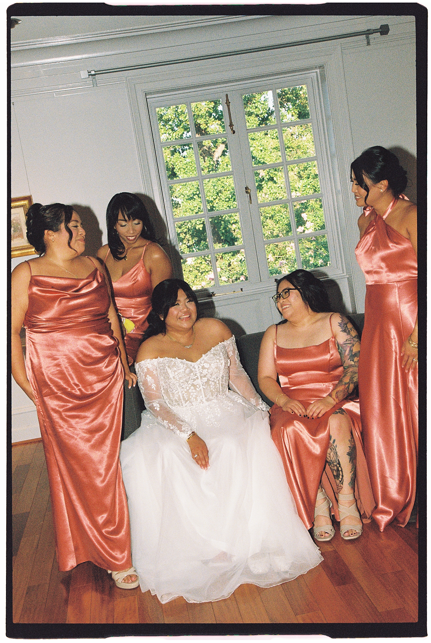 bride in lace gown sits with bridesmaids standing nearby by Maryland wedding photographer