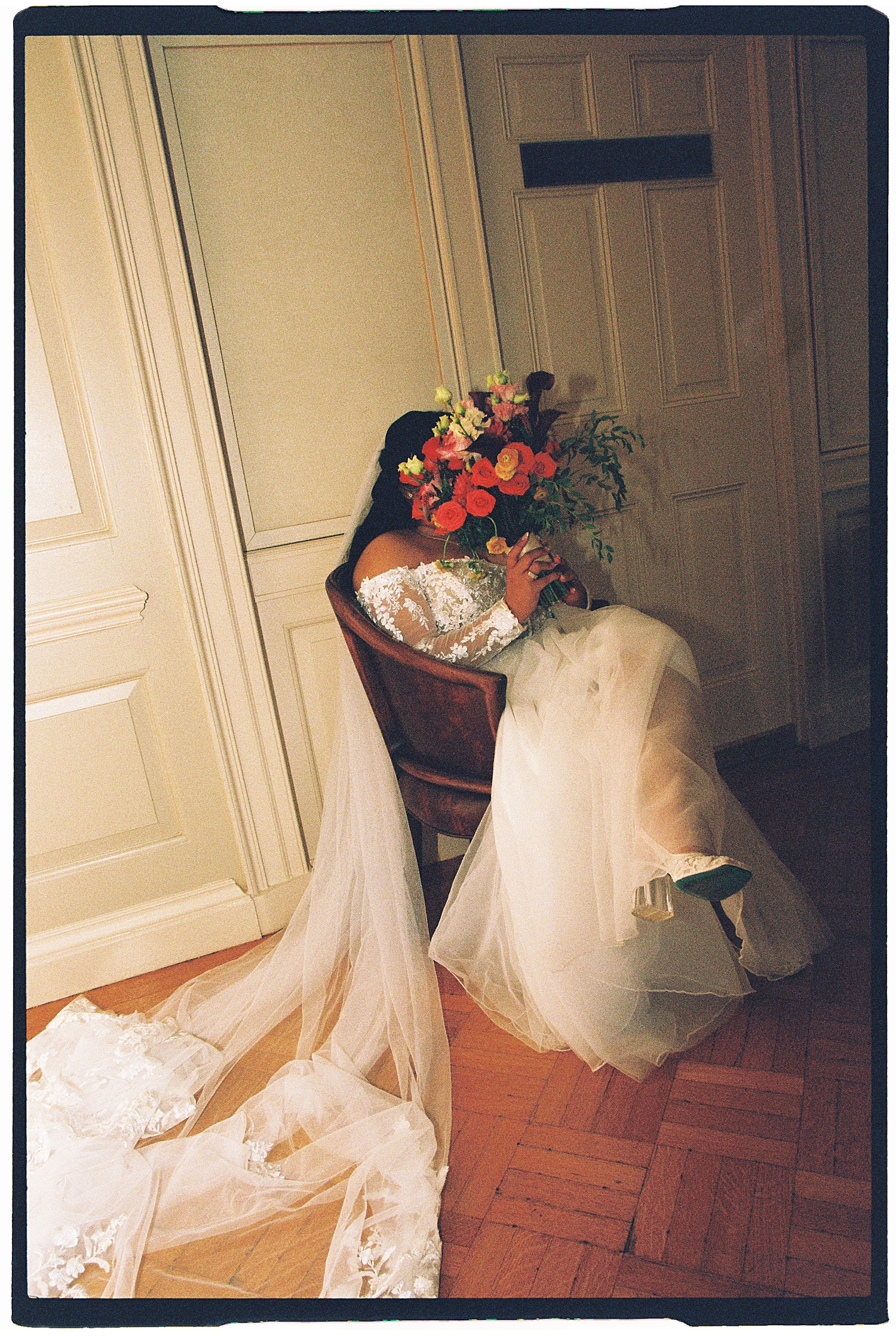 brunette bride sits in chair, covering face with flowers by Sharp Impressions Photography