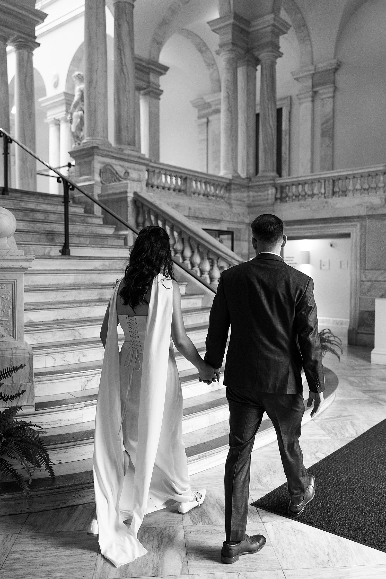man and woman walk hand in hand towards staircase in historic building by Sharp Impressions Photography