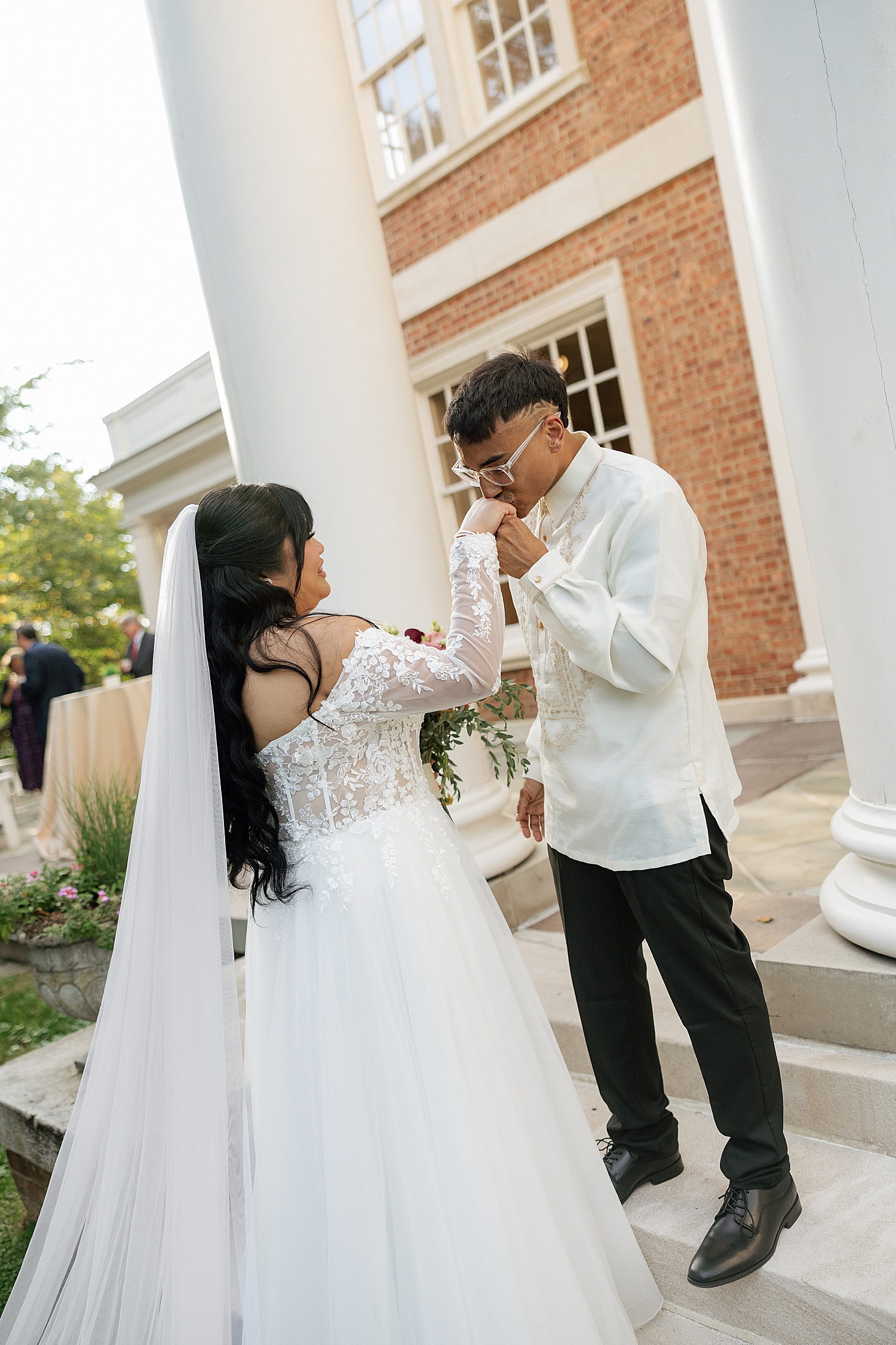 groom in white kisses bride's hand on steps by maryland wedding photographer