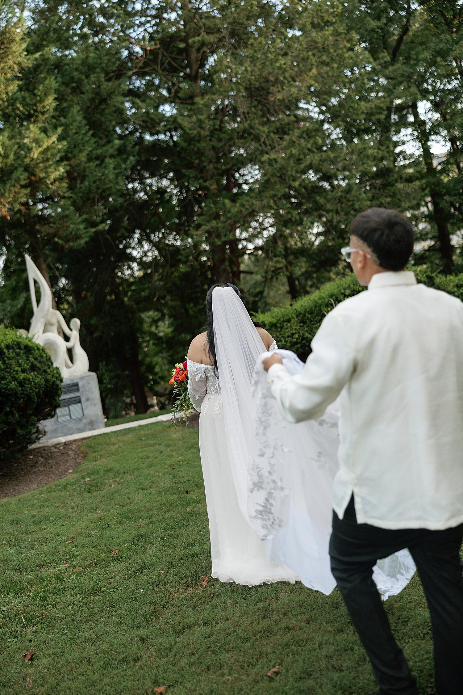 man carries his girl's wedding veil across lawn at The Mansion at Strathmore