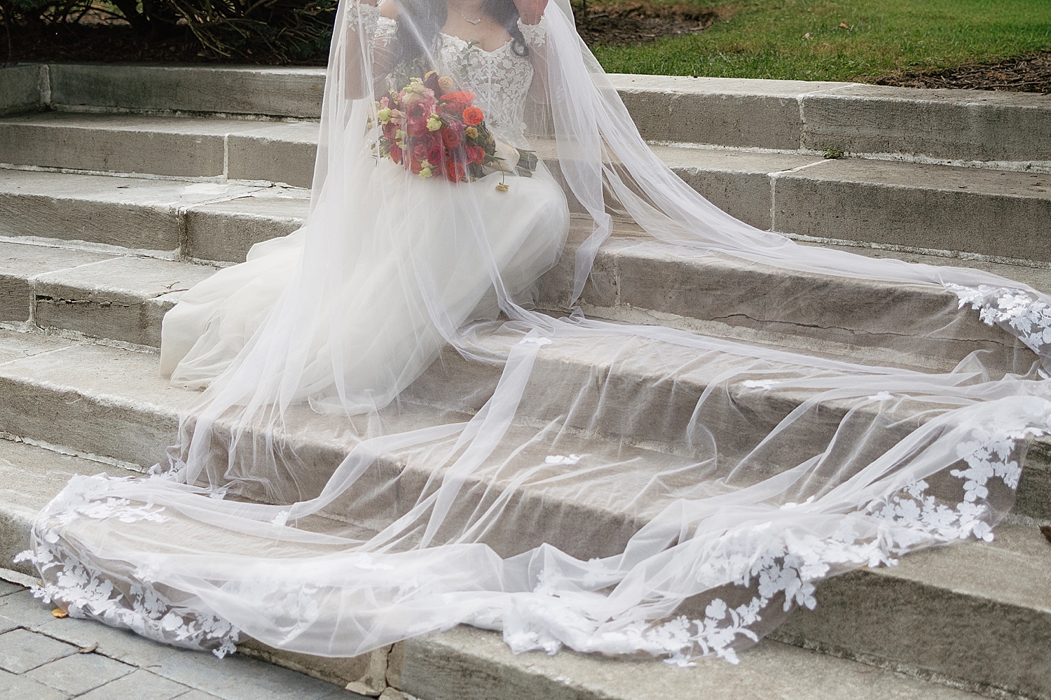 woman sits with her veil surrounding her on steps by Maryland wedding photographer